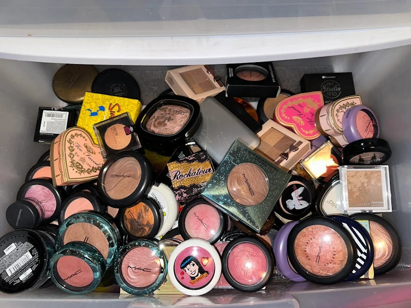 Multiple expired cosmetic products including mascara foundation lipstick being thrown away in trash, makeup audit decluttering process, beauty product safety disposal - InfoProds 2026
