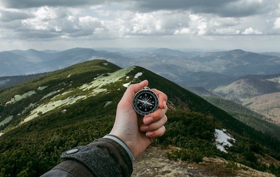 Hiker holding compass at proper chest height level position taking precise bearing measurement to mountain peak demonstrating correct technique for wilderness navigation and orienteering skills - InfoProds 2026