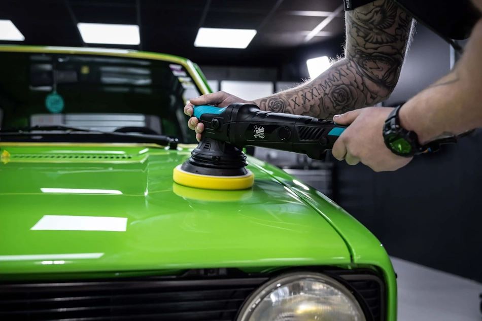 Professional paint correction demonstration showing dual-action polisher with foam cutting pad applying compound to black vehicle panel, removing swirl marks and light scratches through controlled clear coat leveling technique achievable by home detailers following proper safety protocols - InfoProds 2026