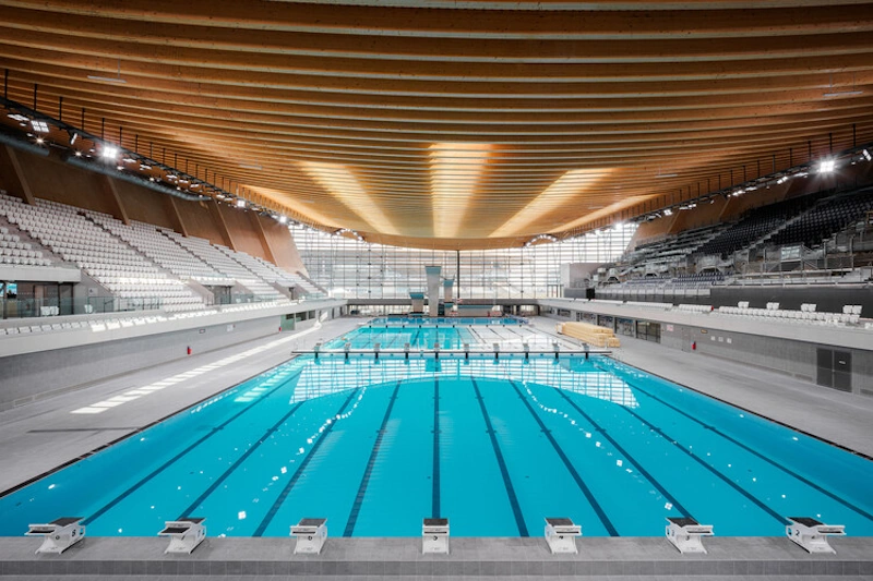 Modern Olympic-standard swimming pool showing advanced perforated gutter systems and specialized lane ropes with wave-dampening technology designed for competitive swimming world record attempts - InfoProds 2026