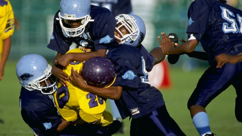 Young children participating in tackle football practice demonstrating early age exposure to repetitive head impacts that research links to increased chronic traumatic encephalopathy risk, with studies showing youth tackle players sustain 15 times more head impacts than flag football participants during equivalent playing time - InfoProds Youth Sports Safety Research 2026