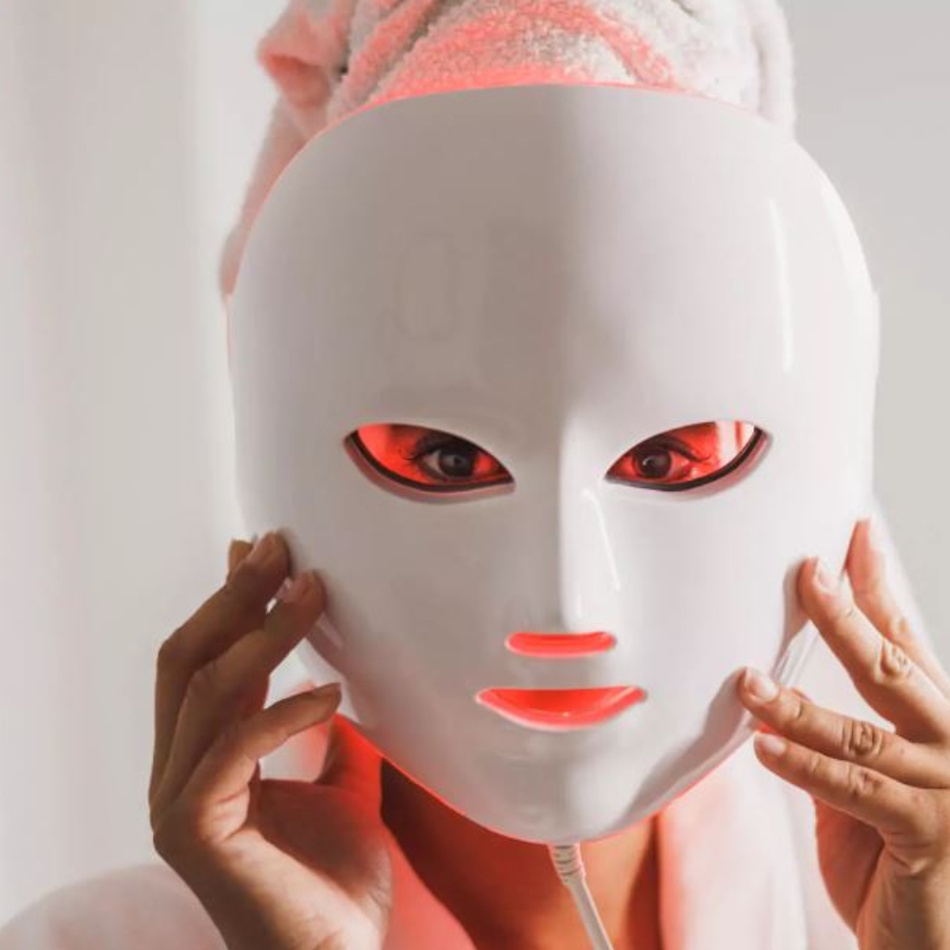 Beautiful woman wearing red LED light therapy face mask in modern spa setting receiving professional photobiomodulation treatment for anti-aging and skin rejuvenation - InfoProds Beauty Guide 2026