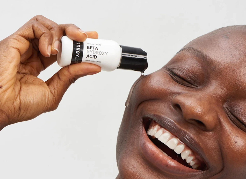 Close-up detailed view of person applying transparent chemical exfoliant serum containing alpha hydroxy acids or beta hydroxy acids to thoroughly cleansed dry facial skin using fingertips demonstrating proper exfoliation night technique in dermatologist-recommended skin cycling routine - InfoProds Beauty Tutorial 202