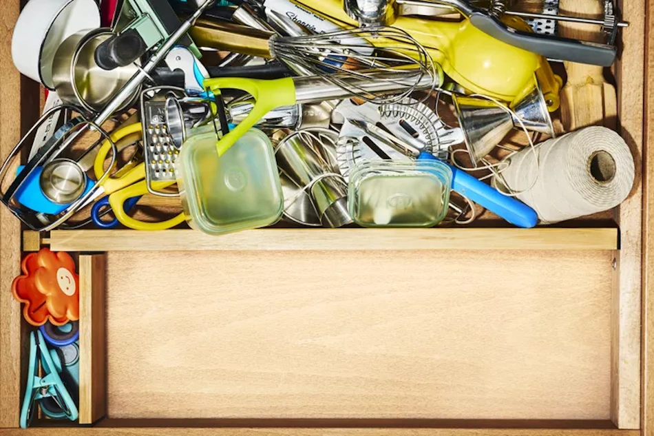 Chaotic disorganized kitchen utility drawer filled with tangled measuring spoons, scattered lids, expired coupons, and miscellaneous items representing the hidden money drain from poor drawer organization - InfoProds 2026 kitchen storage analysis