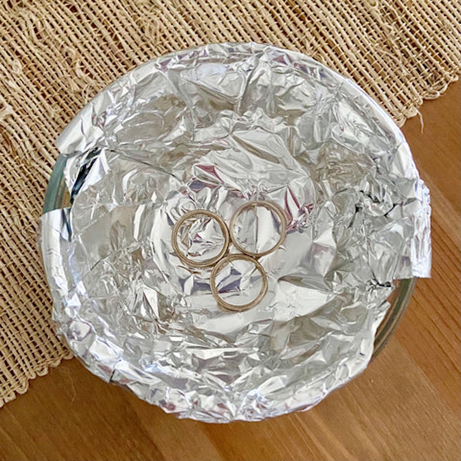 Home chemistry experiment demonstrating electrochemical tarnish removal method with aluminum foil in hot water solution containing baking soda, showing galvanic cell reaction that reduces silver sulfide back to metallic silver without abrasive polishing damage - jewelry restoration InfoProds 2026