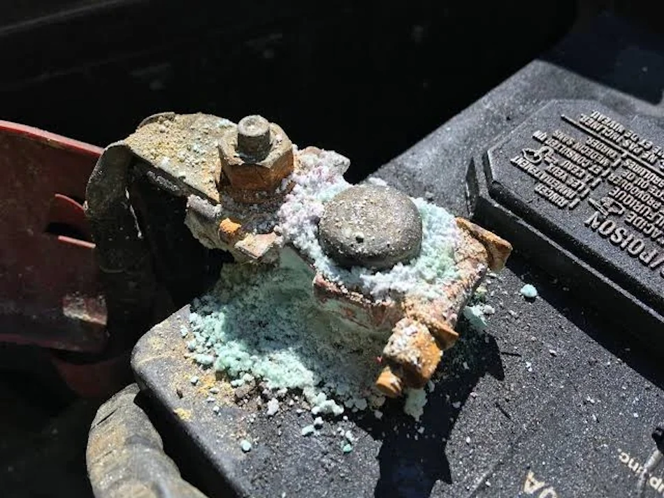 Close-up detailed view of deteriorated automotive jump starter cable clamp connection revealing dangerous green copper carbonate corrosion and white oxidation deposits on electrical contacts creating high-resistance hotspots that cause overheating and fire hazards - InfoProds Car Safety