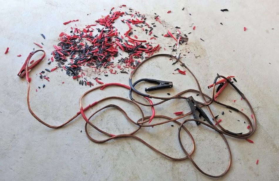 Automotive jump starter cables displaying severe insulation degradation with cracked brittle PVC covering exposing oxidized copper conductor strands demonstrating thermal breakdown and plasticizer loss from high-temperature trunk storage accelerating cable aging - InfoProds Vehicle Electrical Safety 2026