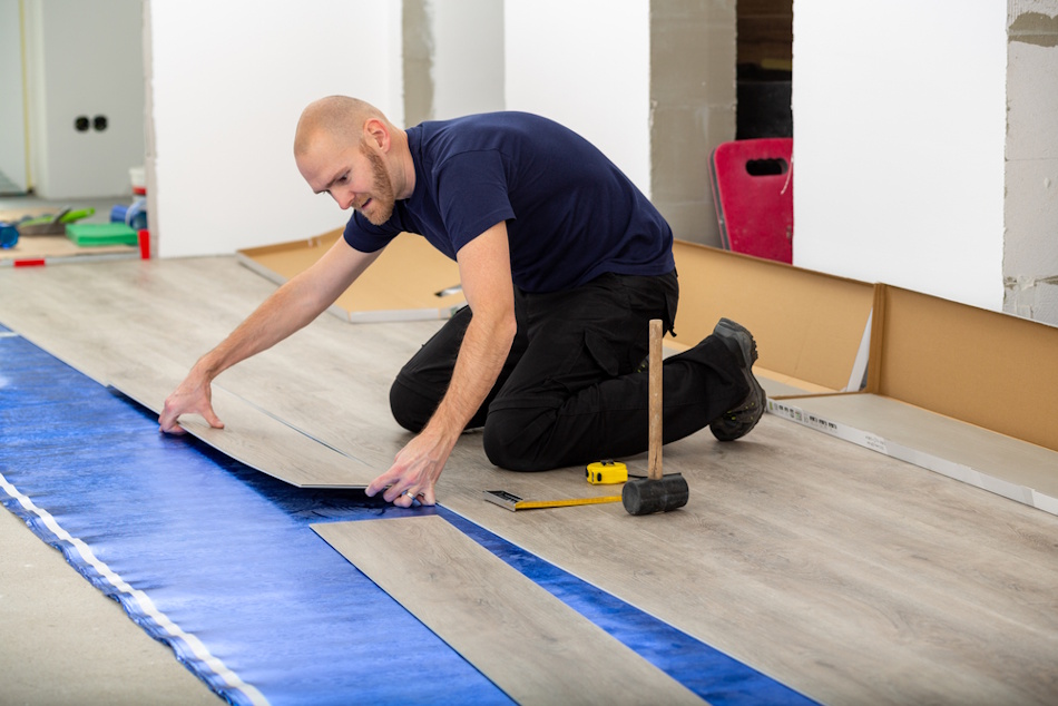 Dense rubber acoustic underlayment material being installed beneath apartment flooring to create impact noise isolation, showing specialized sound-dampening padding that reduces footstep transmission to downstairs neighbors by 15-25 decibels through vibration absorption, essential component of comprehensive apartment soundproofing system - InfoProds 2026