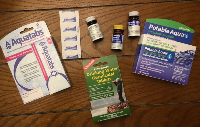 Chemical purification tablets effectiveness testing Water purification tablets including chlorine dioxide and iodine with water bottles showing chemical disinfection testing for bacteria, virus, and parasite elimination effectiveness - InfoProds 2026