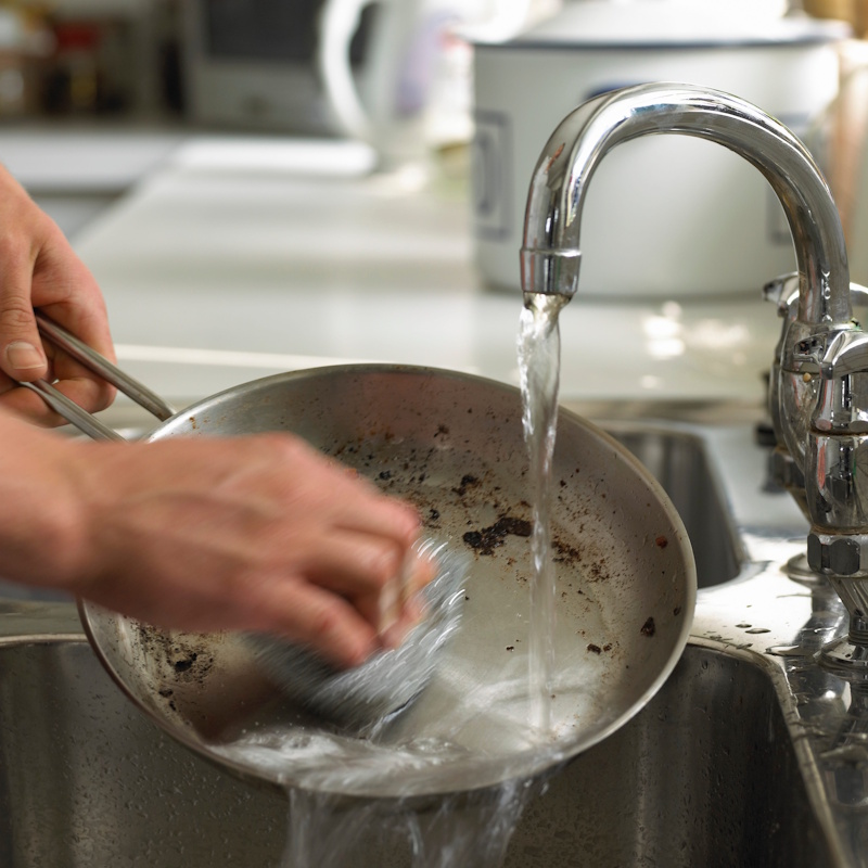 Hands cleaning a shiny stainless steel pan with a soft cloth, demonstrating the easy restoration and maintenance of high-quality kitchen metals for long-term use - InfoProds 2026